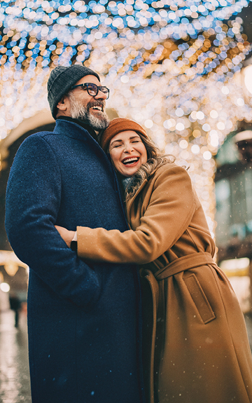 Eine Frau in einem hellbraunen Mantel umarmt einen Mann im blauen Mantel.
