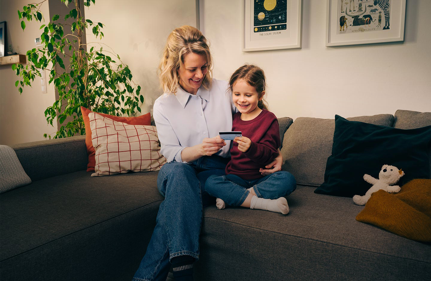 Eine Mutter sitzt mit ihrem Kind auf der Couch, beide halten eine Spar-Karte in der Hand und betrachten diese.
