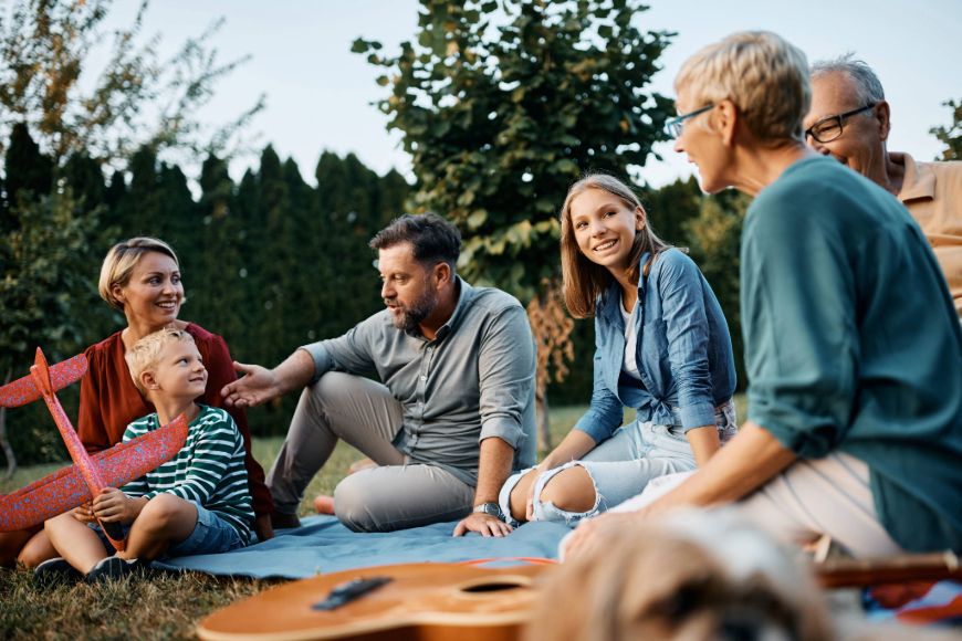 Eine Patchworkfamilie sitzt auf einer Picknickdecke, man sieht auch ein Modellflugzeug und eine Gitarre.