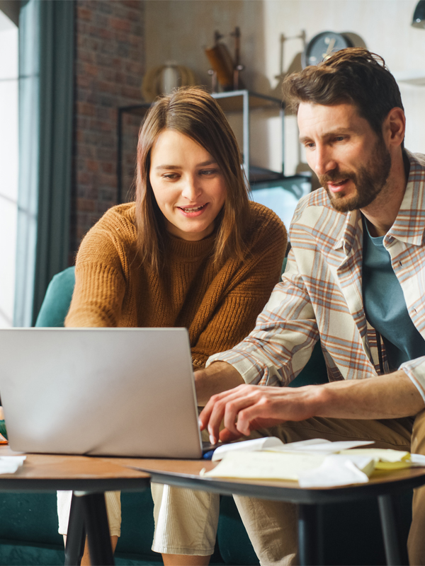 Ein Mann sitzt mit seiner Frau vor dem Laptop und gibt was ein.